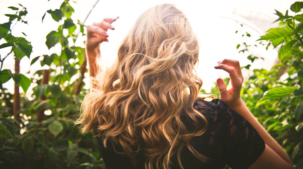 blonde haired woman in black top surrounded by tall plants | How To Get Loose Curls Without Going To The Salon | how to get loose curls | Featured
