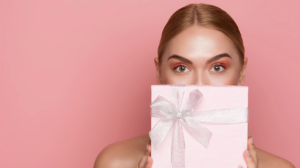 Beautiful woman with eye makeup and nude shoulders covering lower face with gift box | The Best Holiday Makeup Gift Sets of 2019 | Makeup Gift Sets 2019 | Holiday makeup sets 2019 | Featured