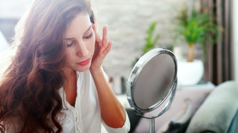 young woman looking in the mirror | Secrets To Get Glowing Glass Skin | glass skin | Featured