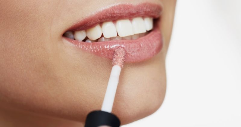 young woman applying lip gloss | Wayne Goss Cosmetics, Is It Worth It?