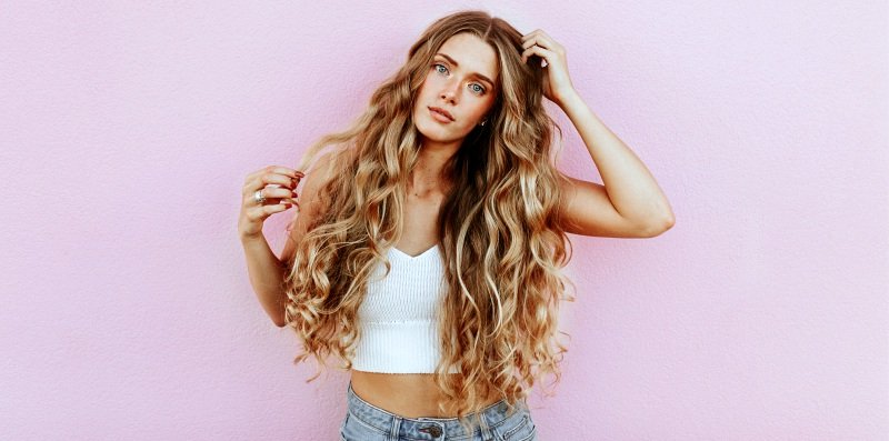 woman with long curly hair with pink background | Trendy Fall Hair Colors To Update Your Look For The Season