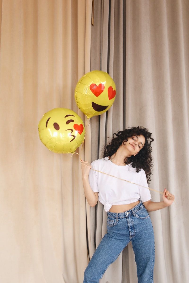 woman in white shirt and blue denim shorts holding yellow and red balloons | Natural hairstyles for short hair