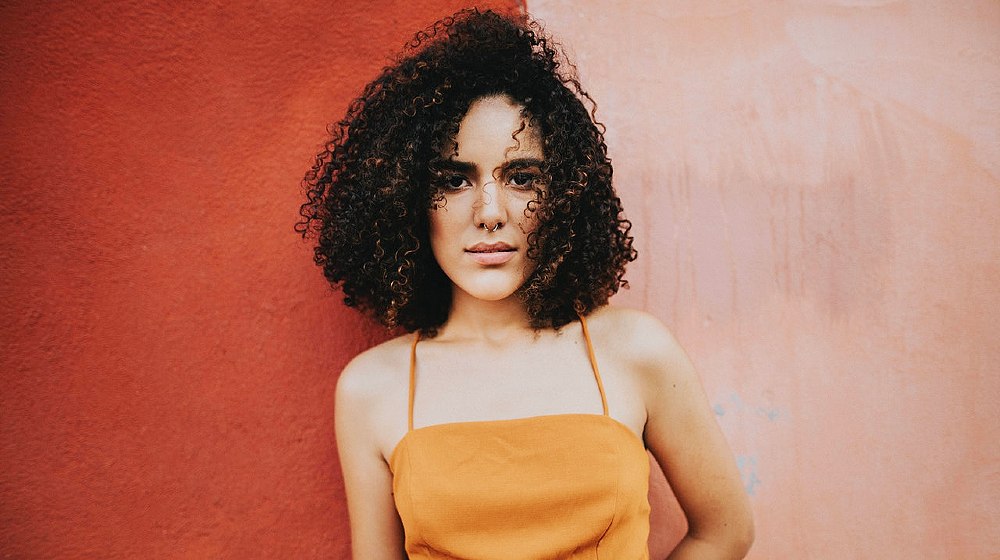 woman wearing an orange top standing beside pink wall | How To Properly Take Care 3C Curly Hair Type | Featured