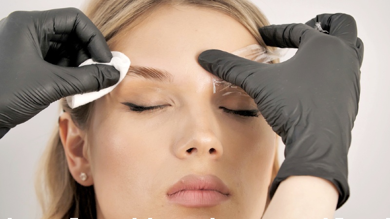 stylists hand in black gloves wipe the face of the model with a cotton pad | brow lamination steps