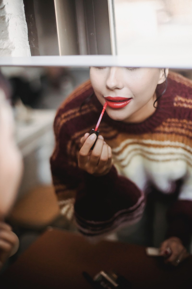 woman applying red lipstick while preparing for event | best long-lasting lip gloss