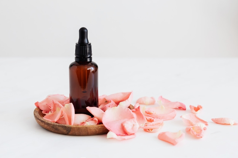 essence bottle put on wooden plate near rose petals | organic collagen serum