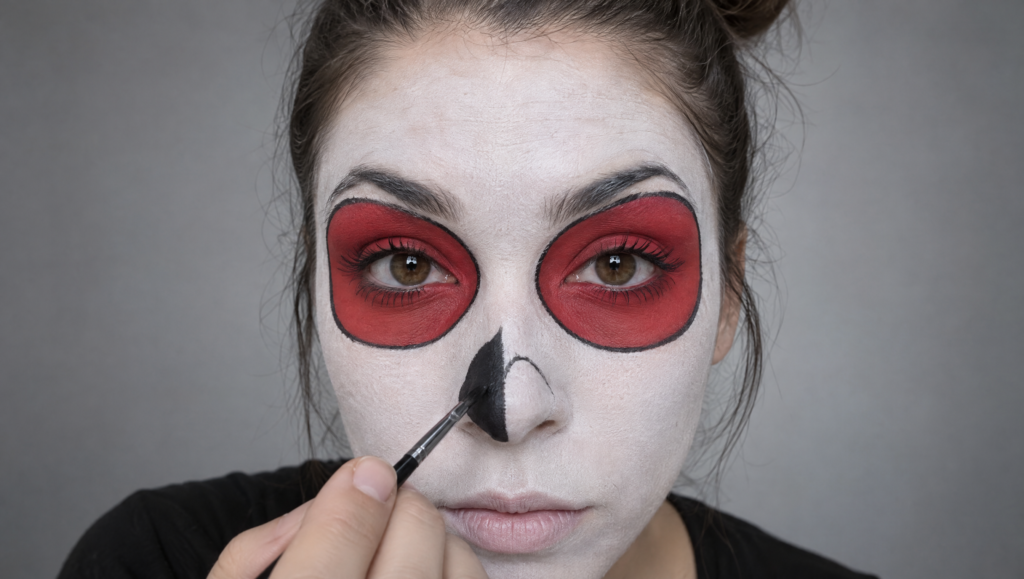 Day of the Dead makeup tutorial step 6: fine brush filling in a black upside-down heart shape on the nose