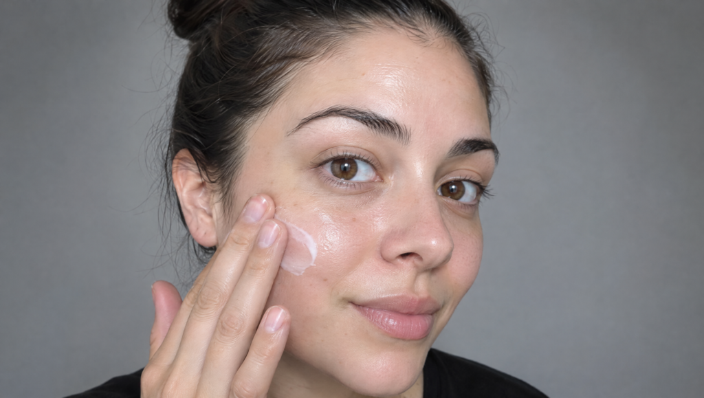 Day of the Dead makeup tutorial step 1: bare face with moisturizer being patted onto the cheek